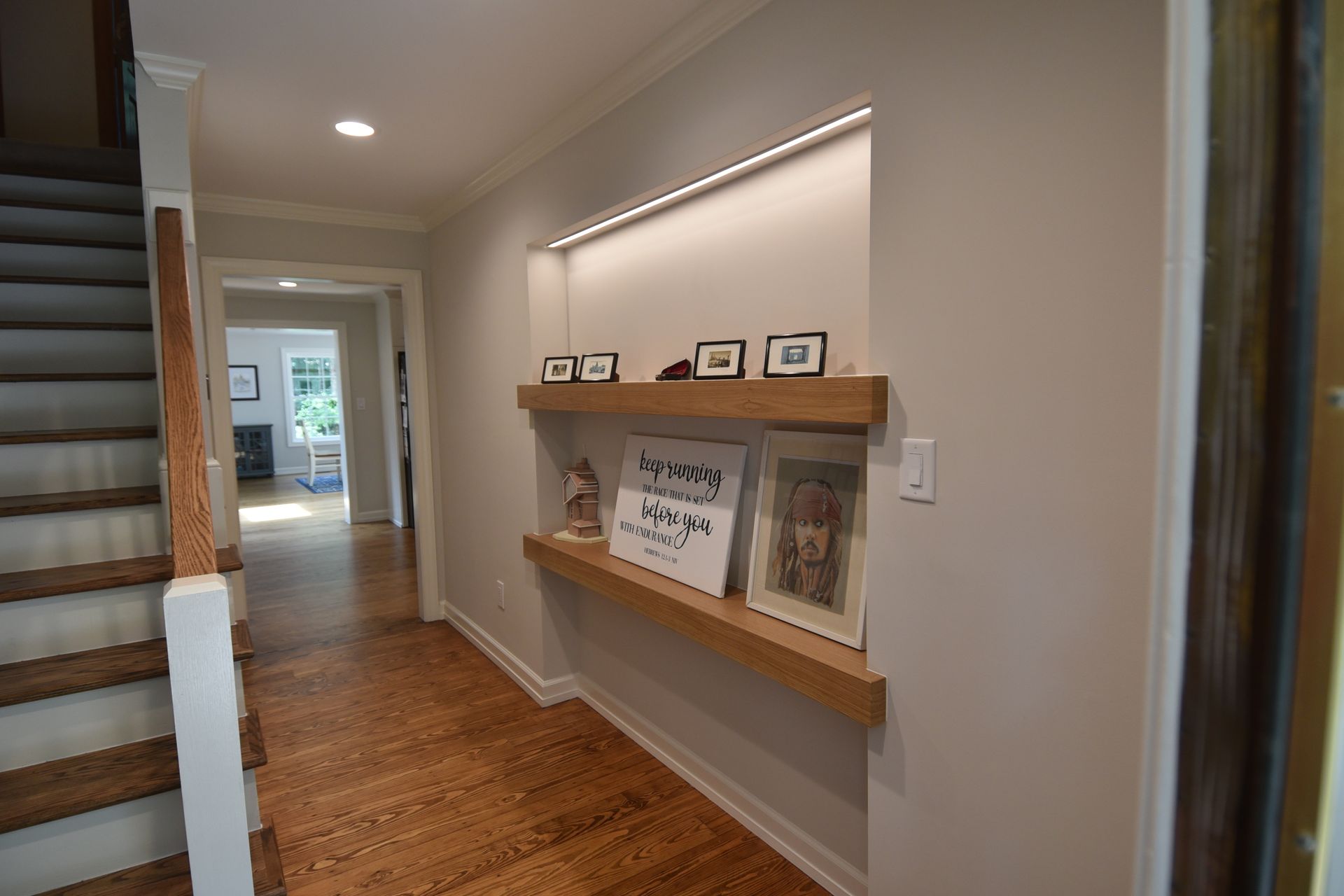 Entryway with wooden floors, recessed shelf with art, stairs on the left, and a doorway to a room.
