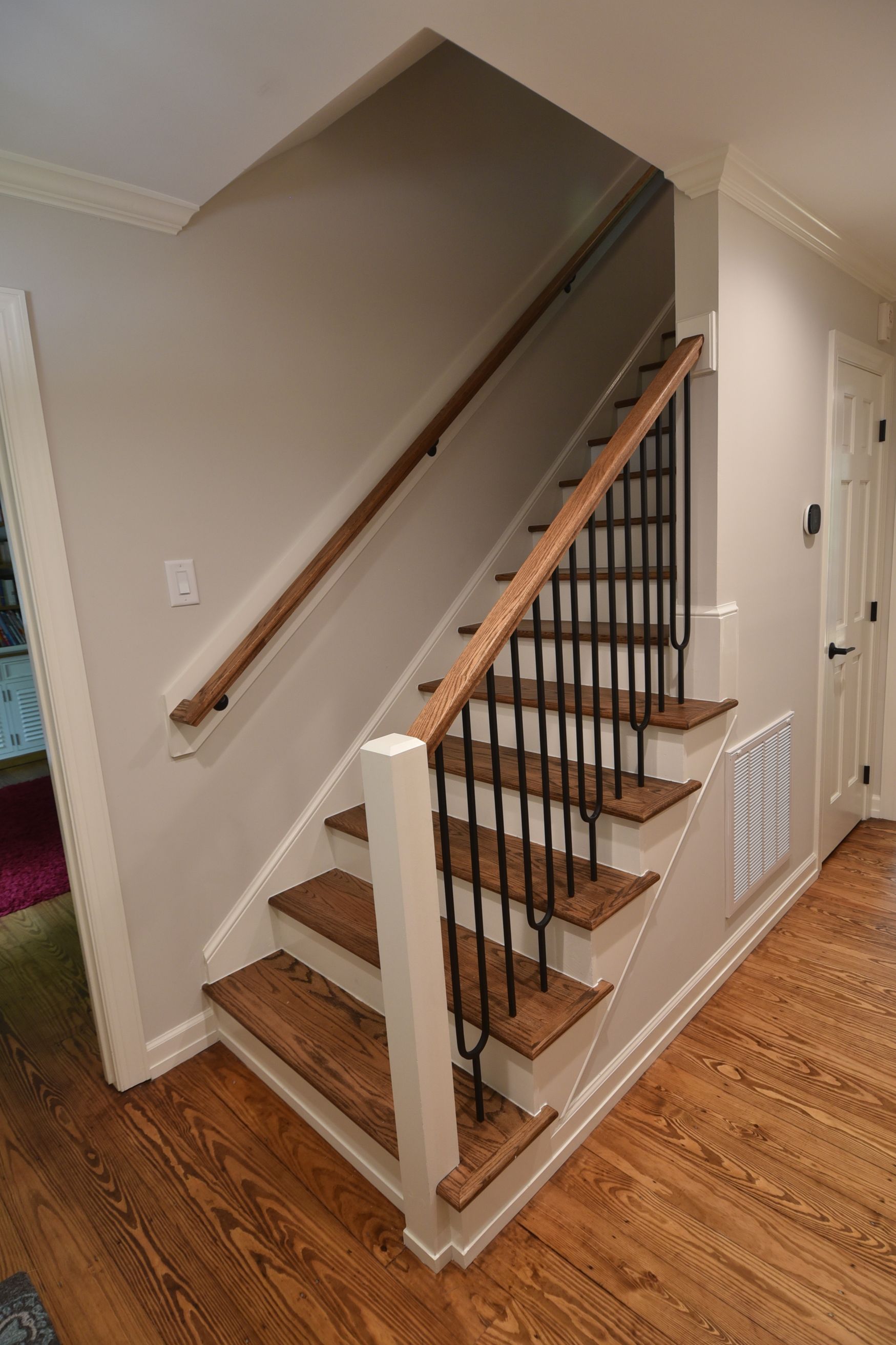 Staircase with wooden steps, dark metal spindles, and wood handrails against light gray walls.