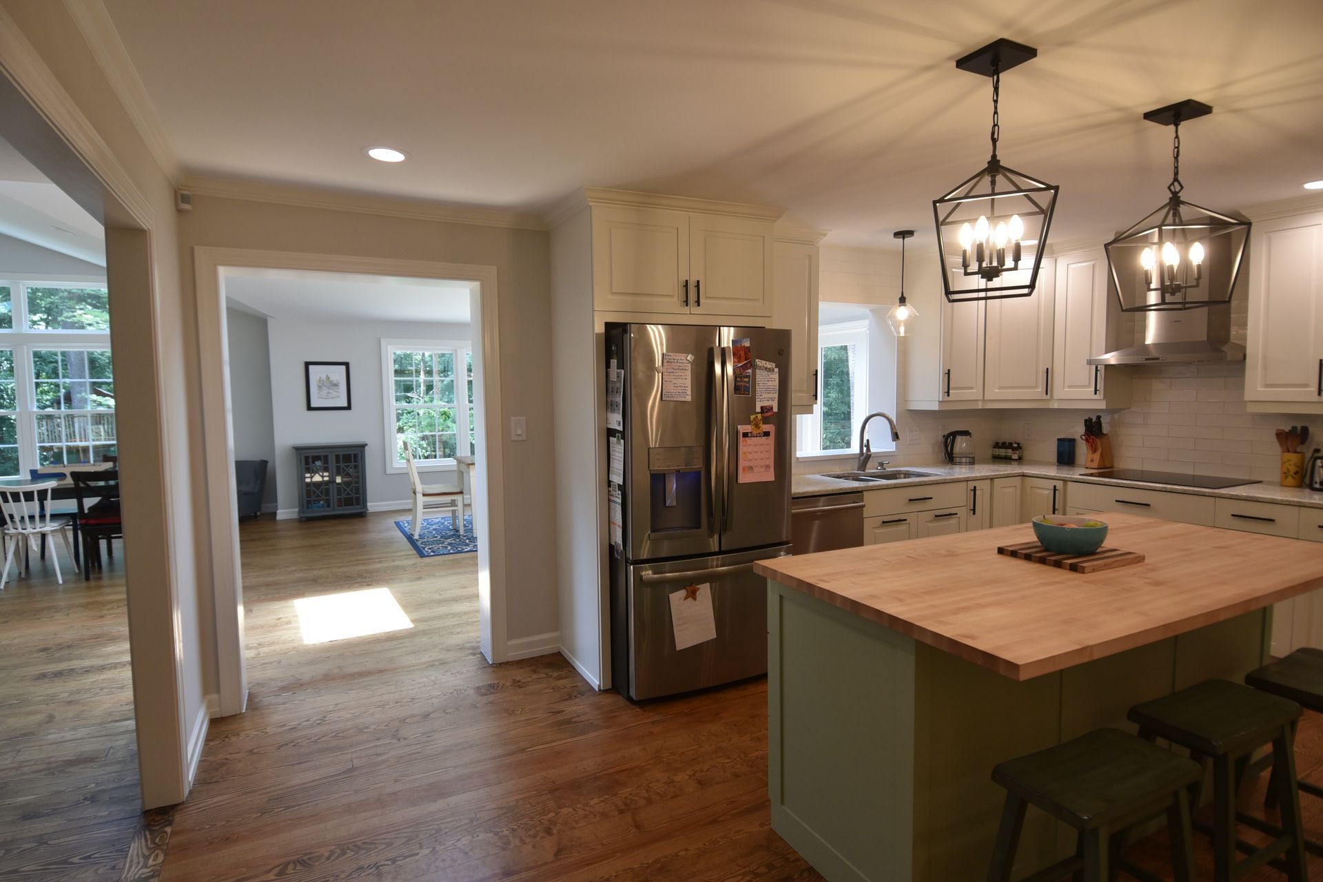 A modern kitchen with an island, stainless steel fridge, and a view into the dining room.