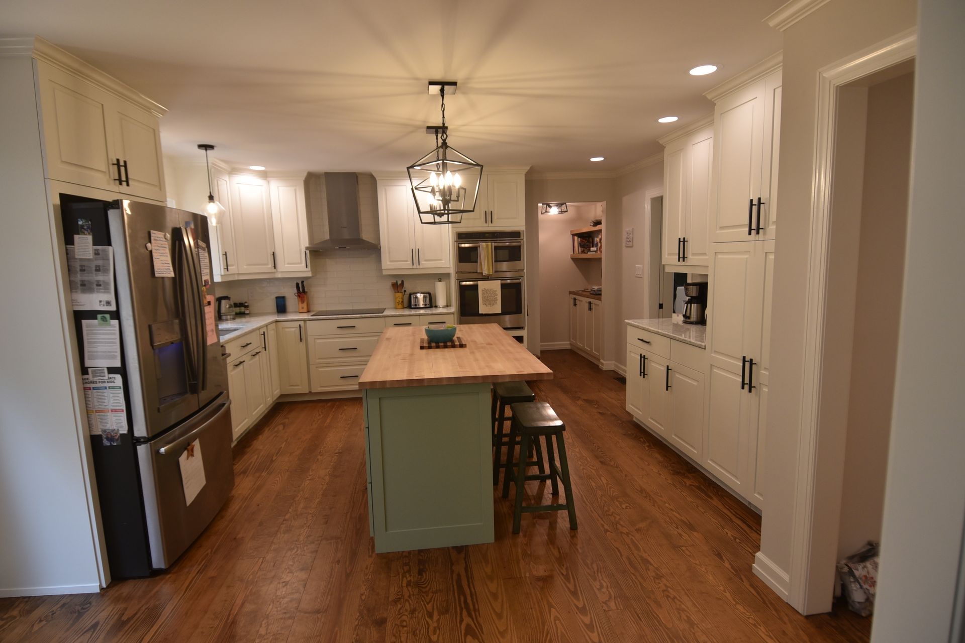 Spacious kitchen with light cabinets, wood floor, green island, and stainless steel appliances.