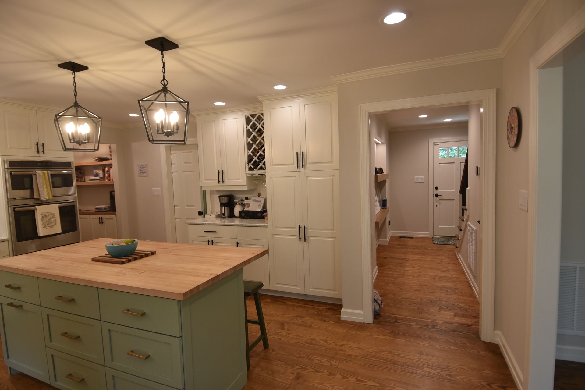 A kitchen with a green island, white cabinets, hardwood floors, and pendant lights.