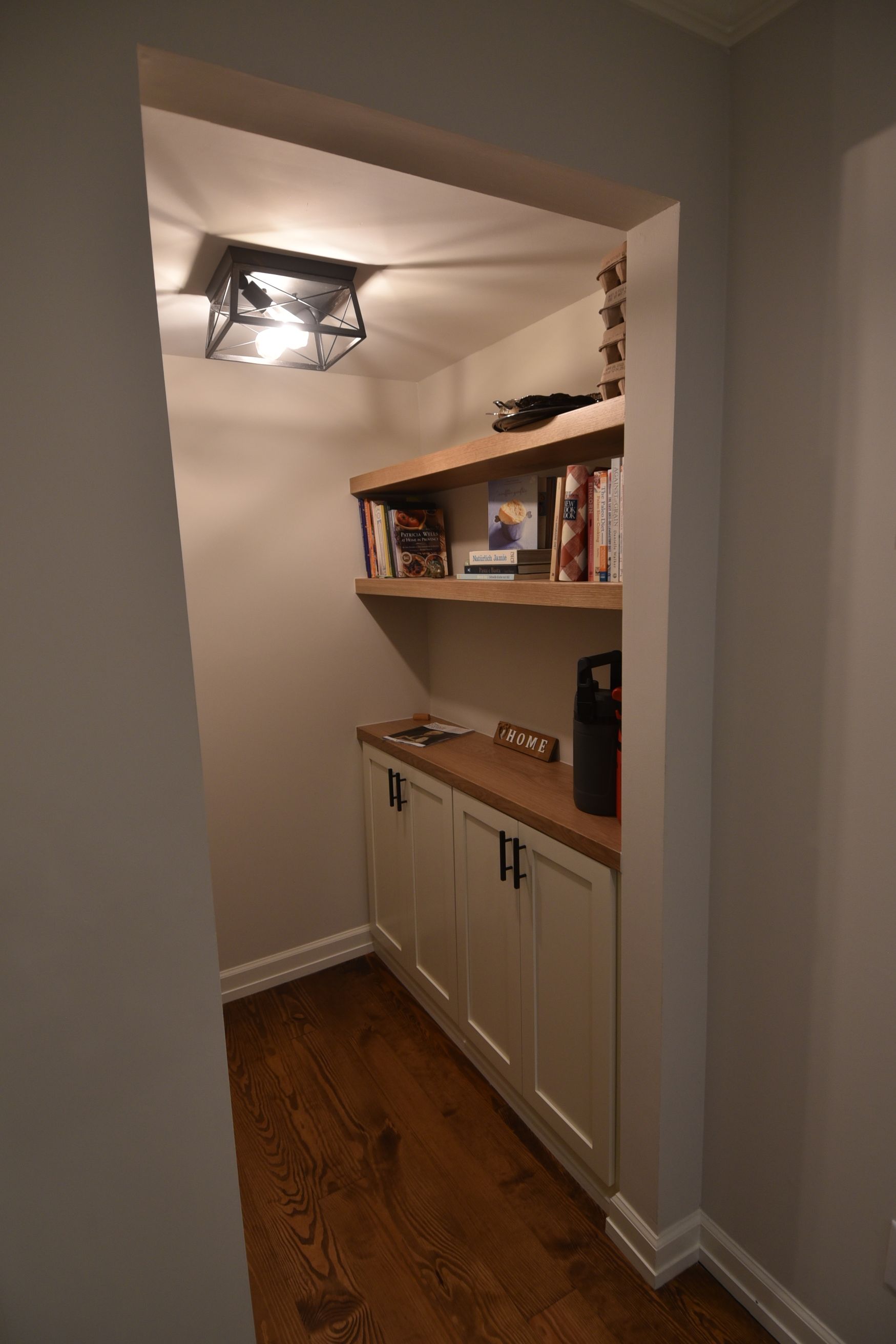 Built-in alcove with shelves, cabinets, and light fixture; stained wood and white cabinetry with books.