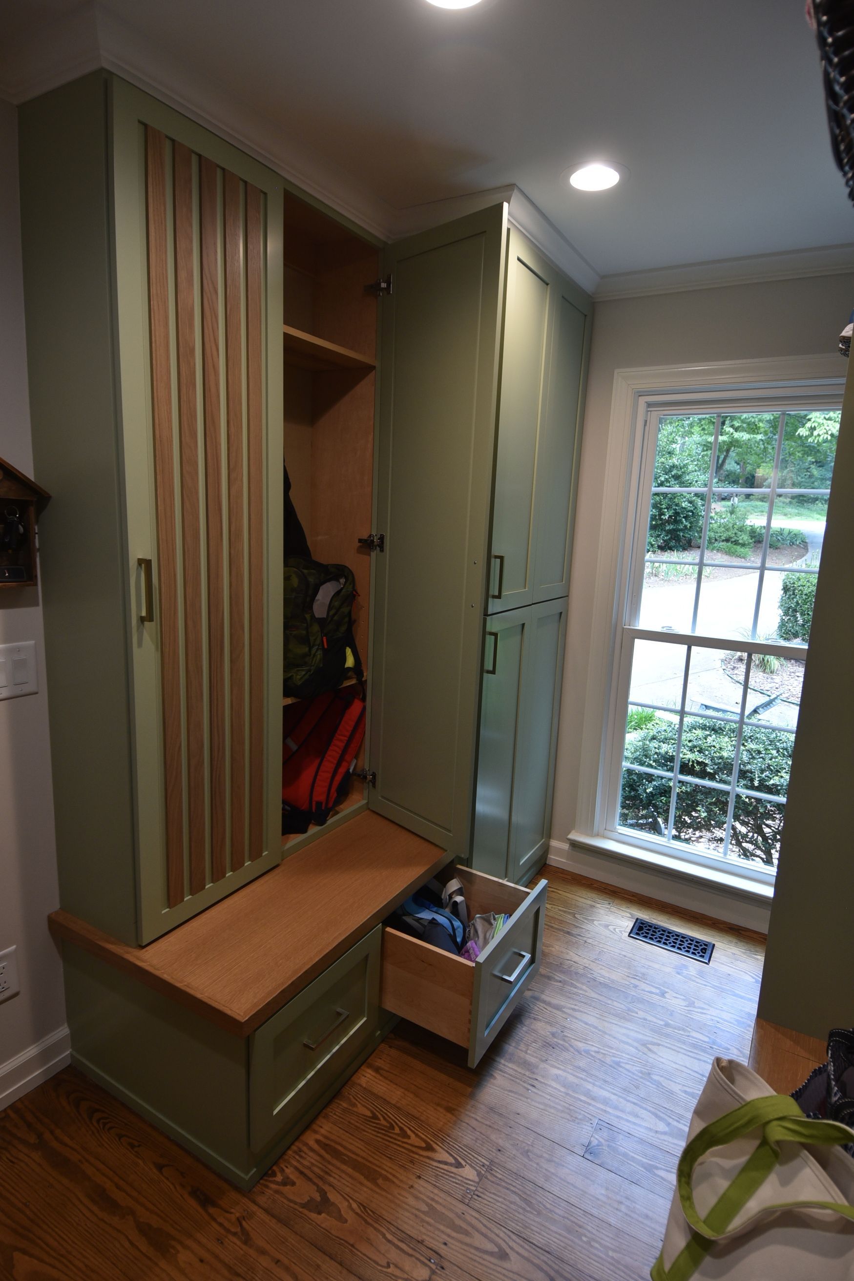 Built-in entryway storage with green cabinets, a bench, and wood grain accents. A window with a view is on the right.