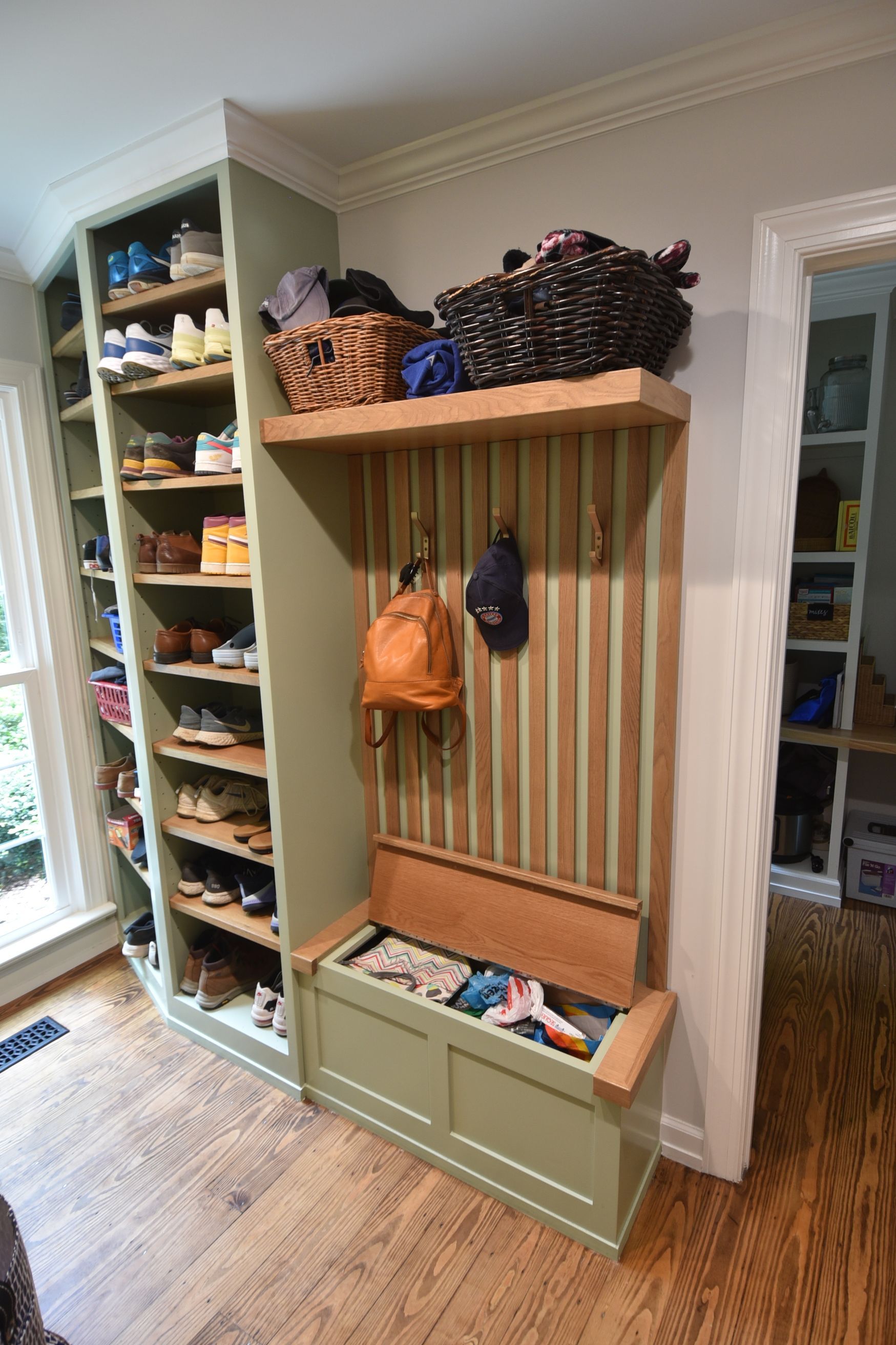 Green entryway storage unit with shoe shelves, coat hooks, and bench, with baskets on top.
