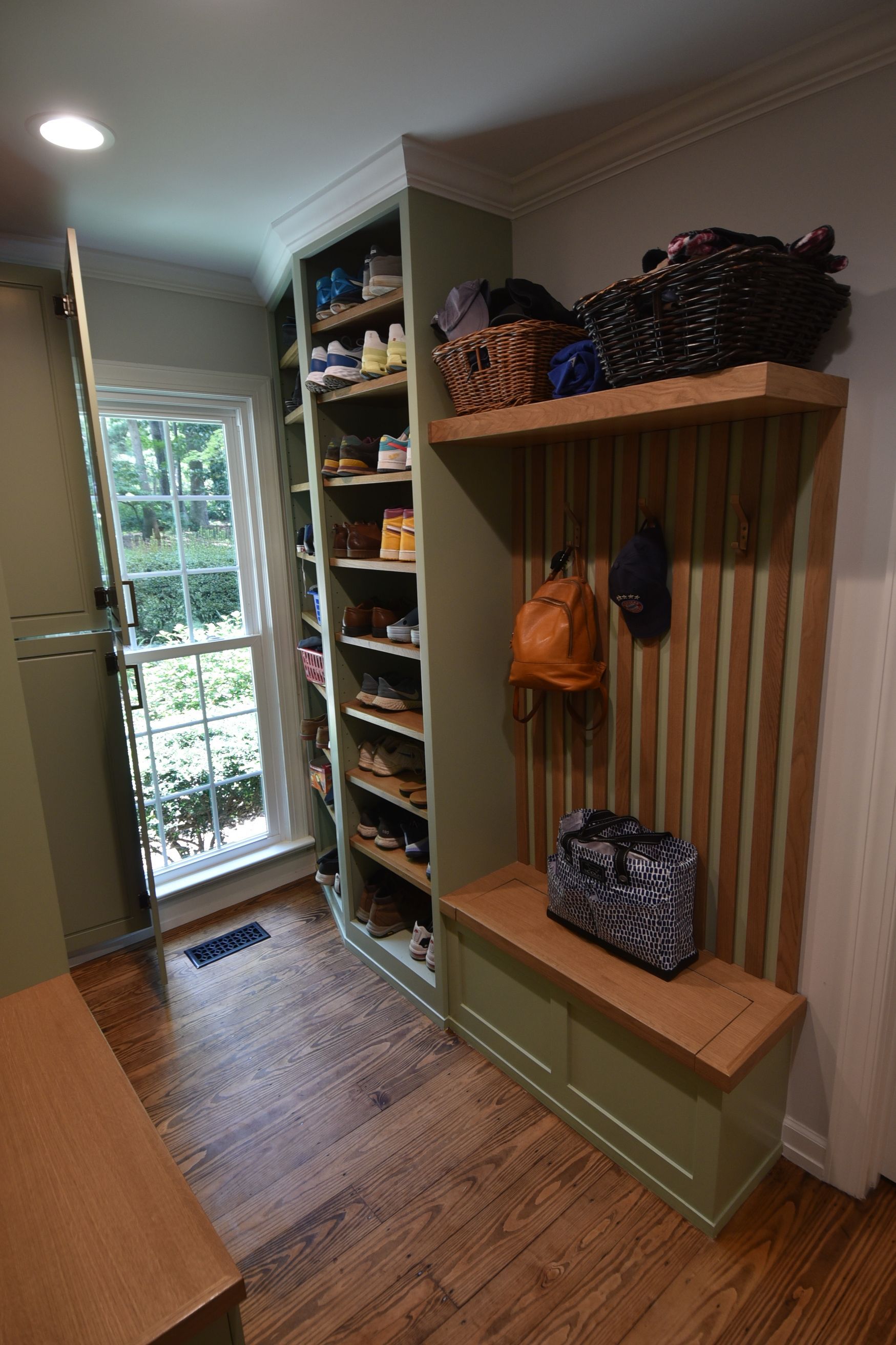 A mudroom with a shoe rack, bench, and hooks in a green and wood tone color scheme.