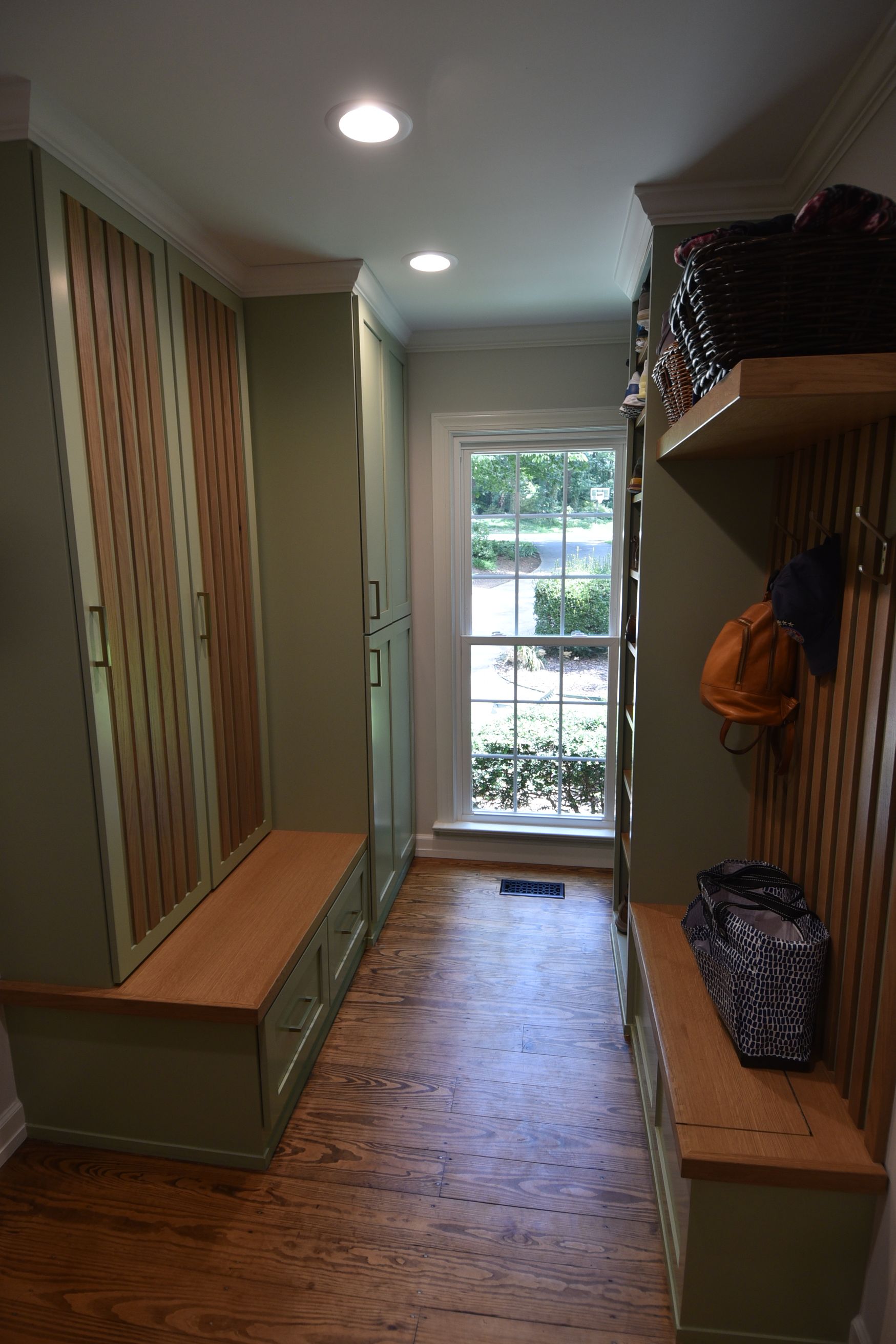 A narrow hallway with custom green and wood storage cabinets and a window at the end.