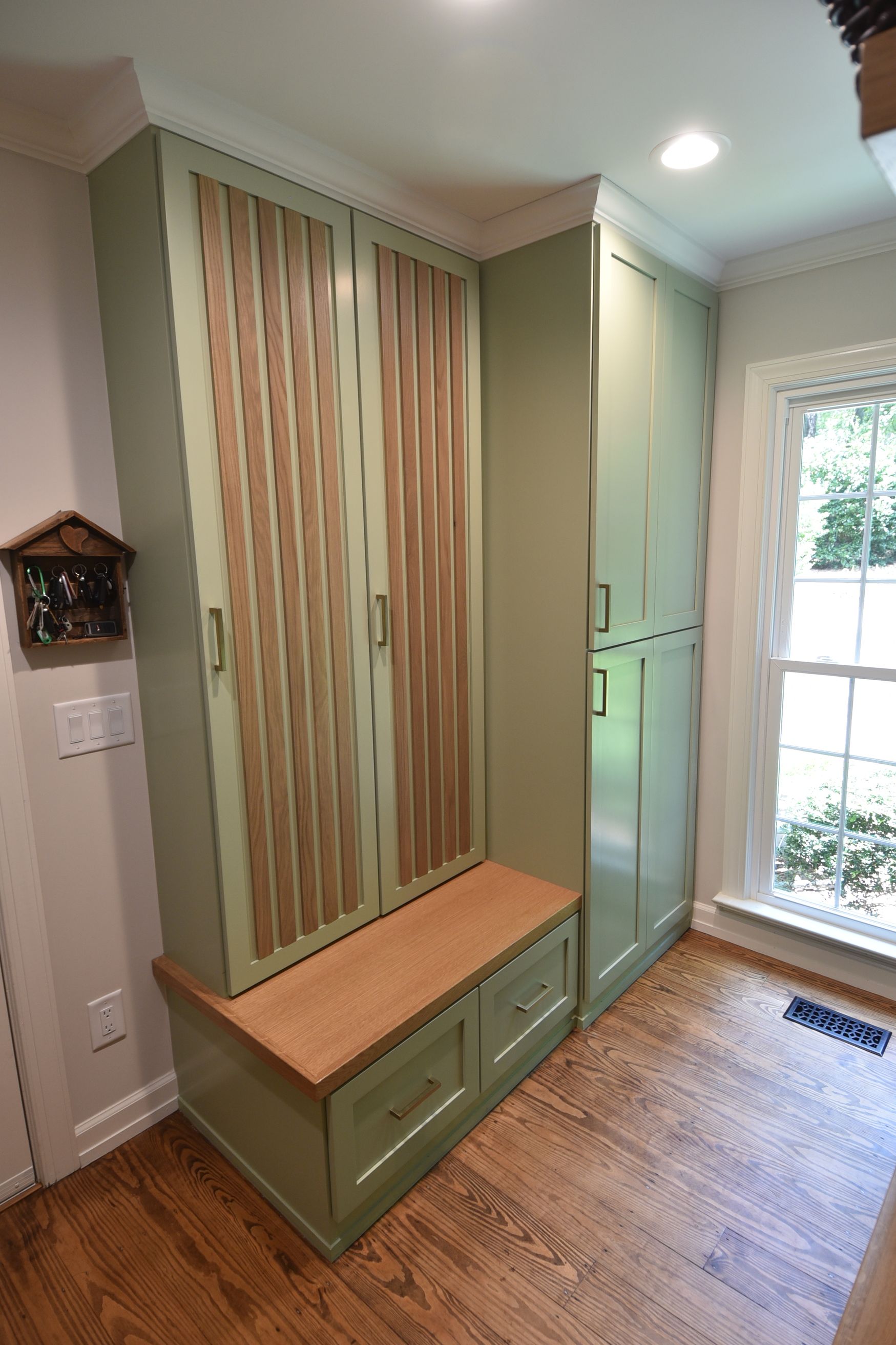 Green and wood tone built-in storage with bench in a room with a window.