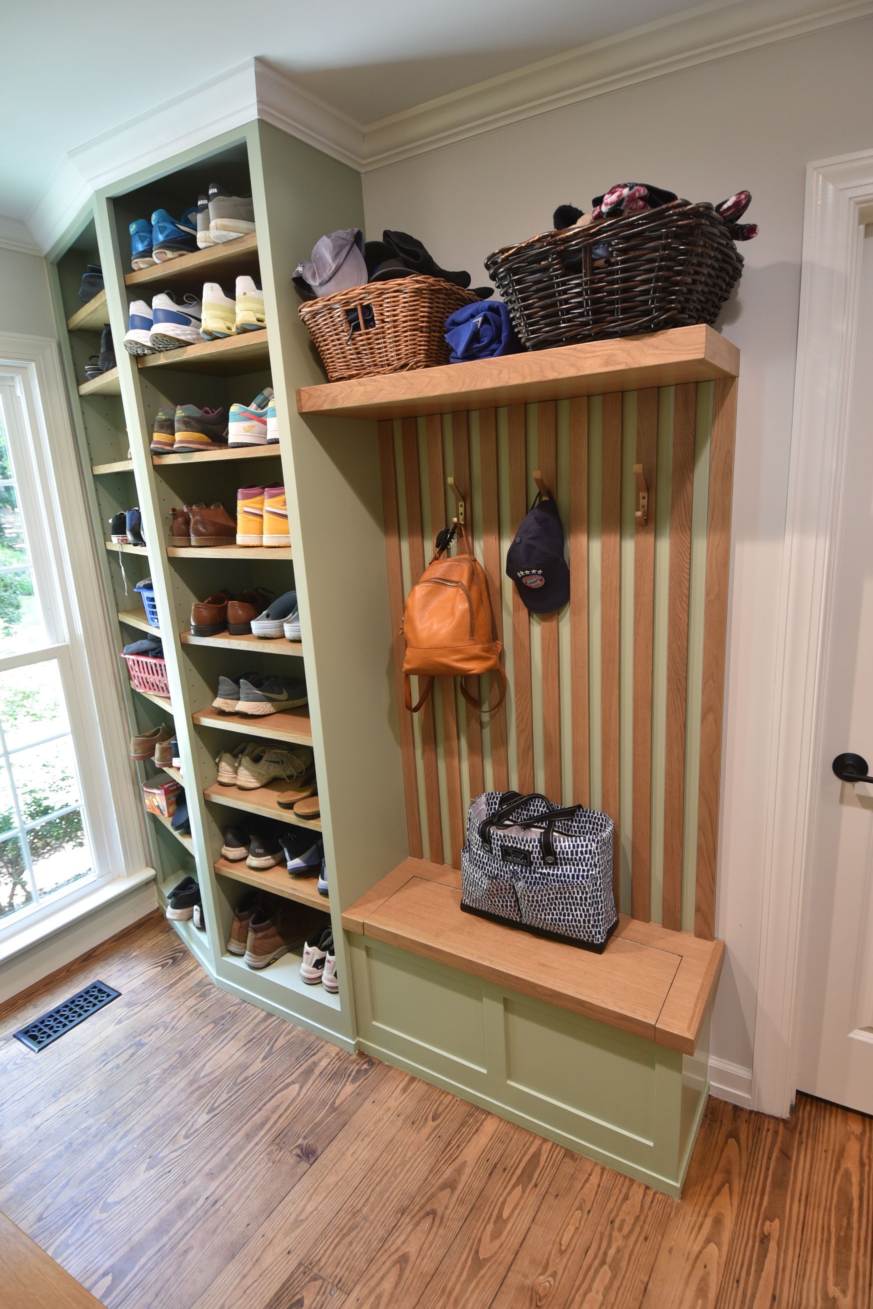 Built-in entryway storage: shoe shelves, coat hooks, bench. Green cabinetry, wood shelves, baskets, and bags.