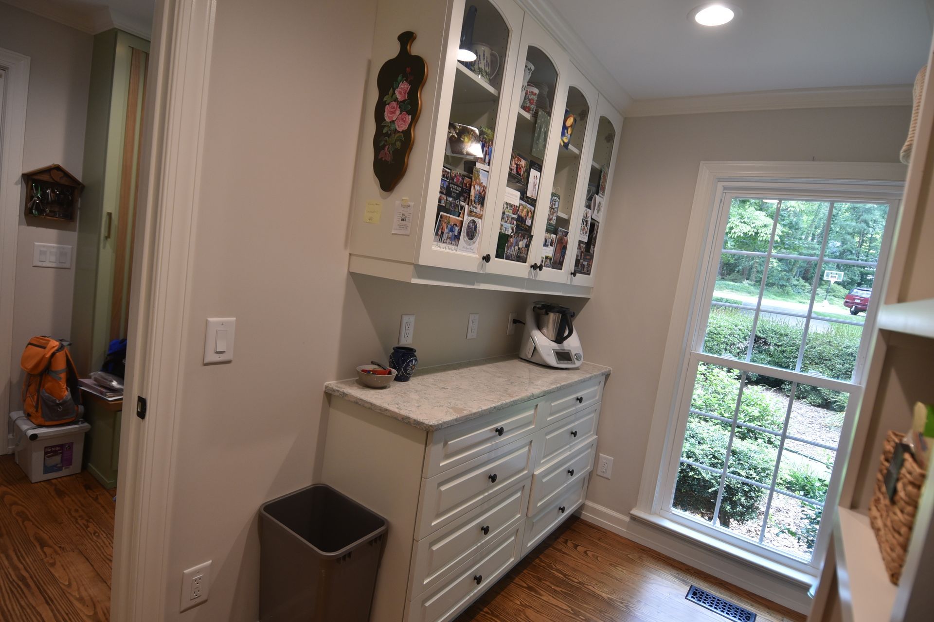 Kitchen nook with white cabinets, window, and a trash can.