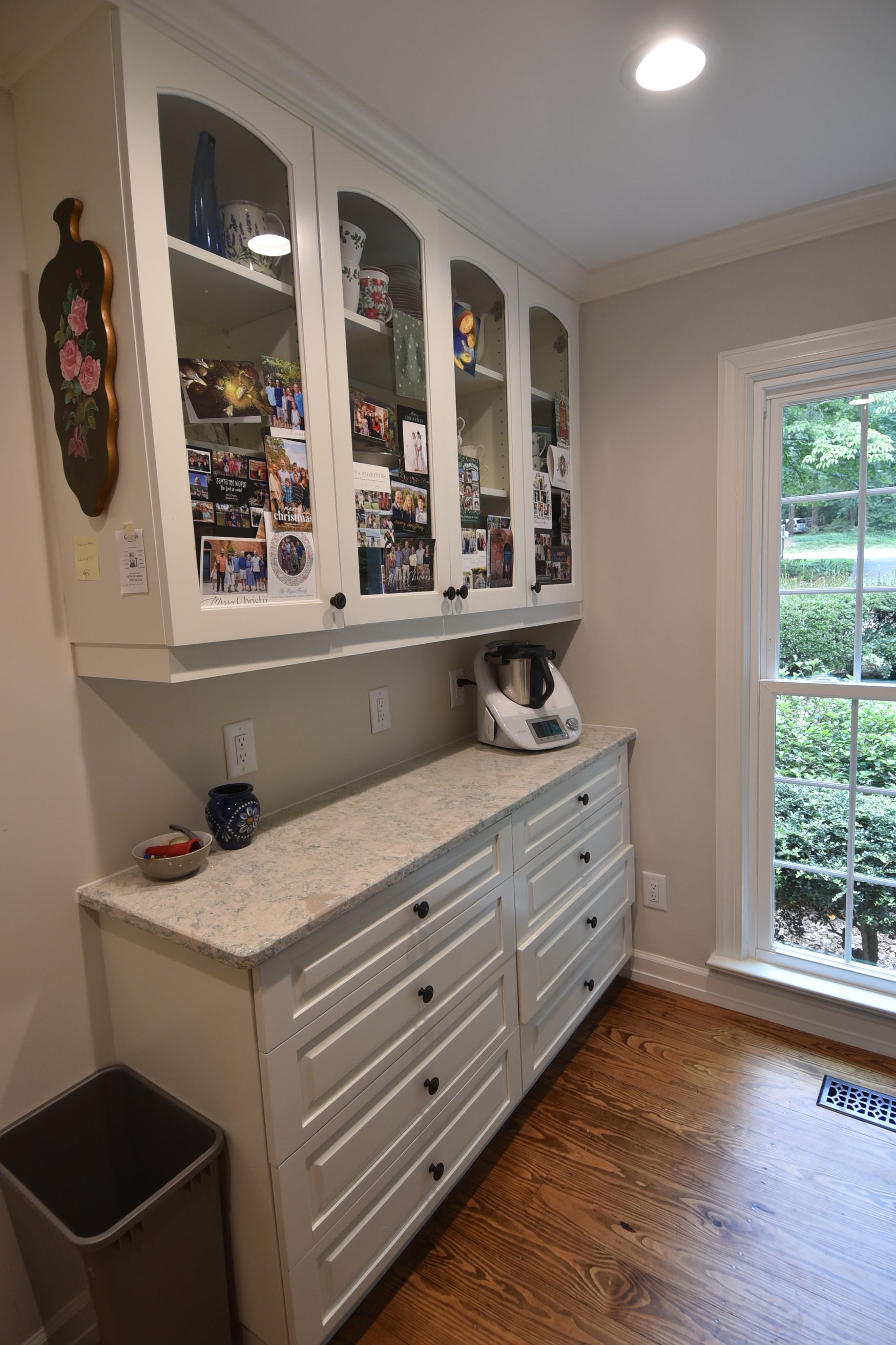 White cabinets with countertop, drawers, and display area; near a window with a view of trees.