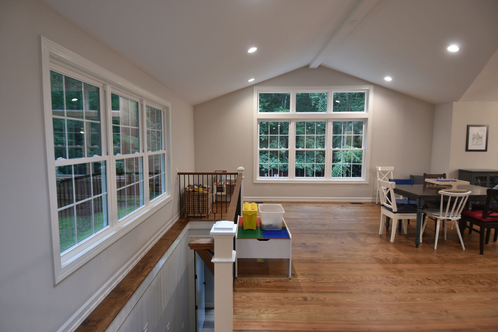 Bright playroom with large windows, hardwood floors, and a small balcony overlooking a stairwell.