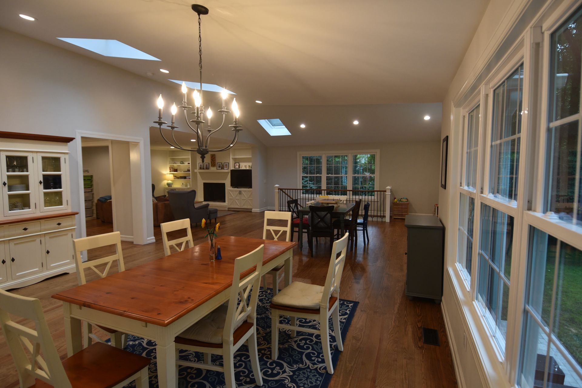 Dining room with table, chairs, chandelier, and windows. Fireplace and living area in background.