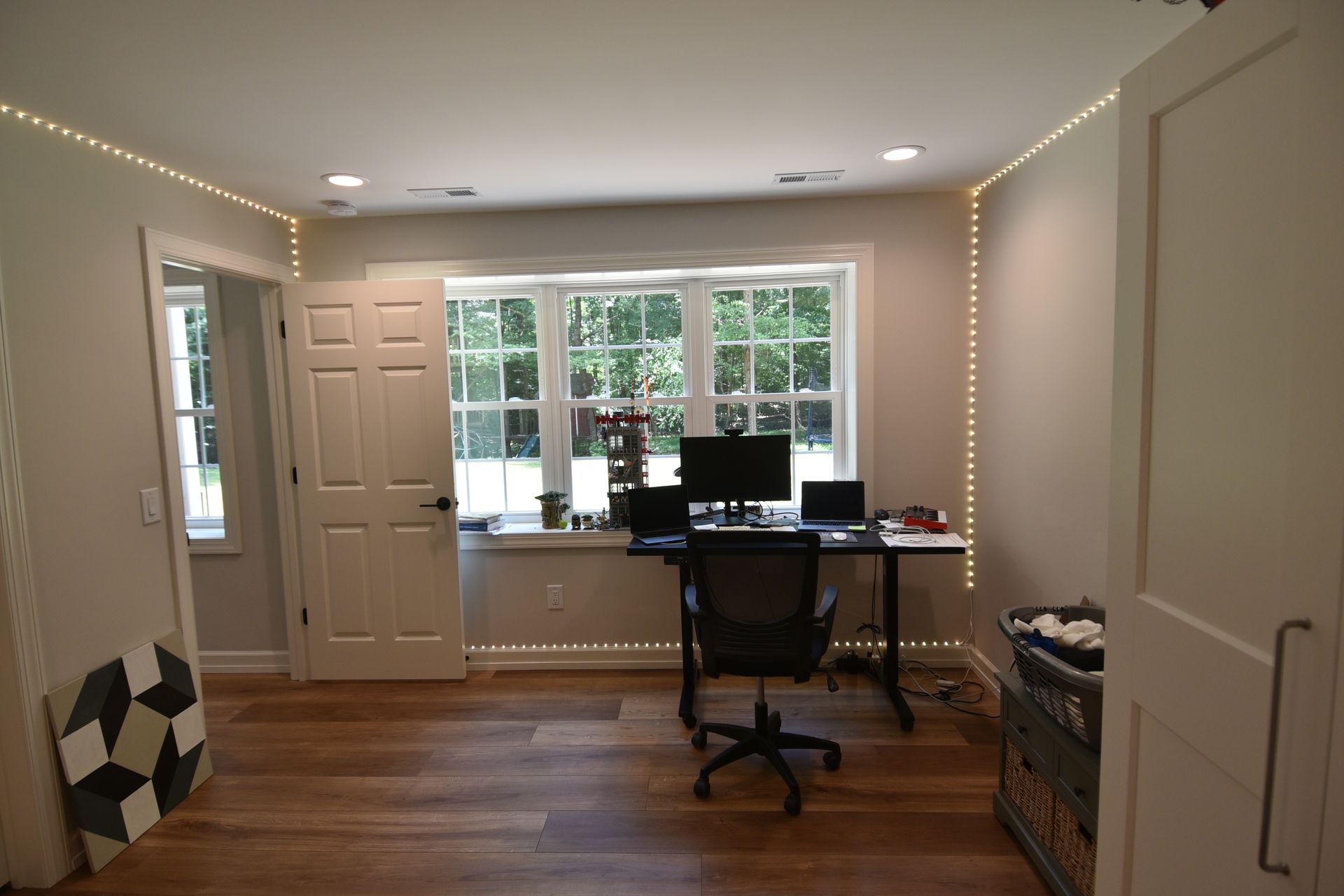 Home office with desk, chair, window, wood floor, and string lights.