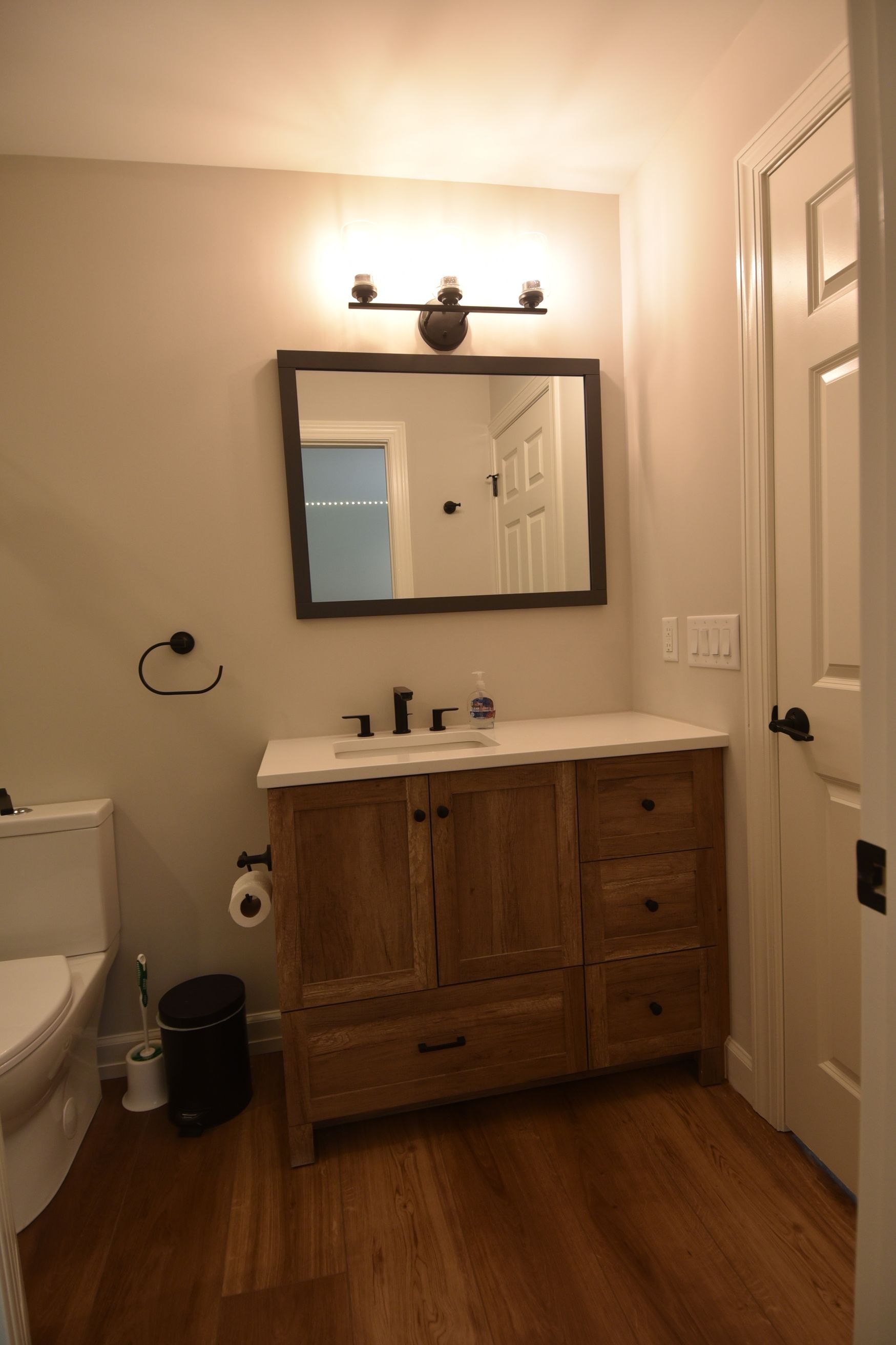 Bathroom with wooden vanity, mirror, toilet, and brown hardwood floors.