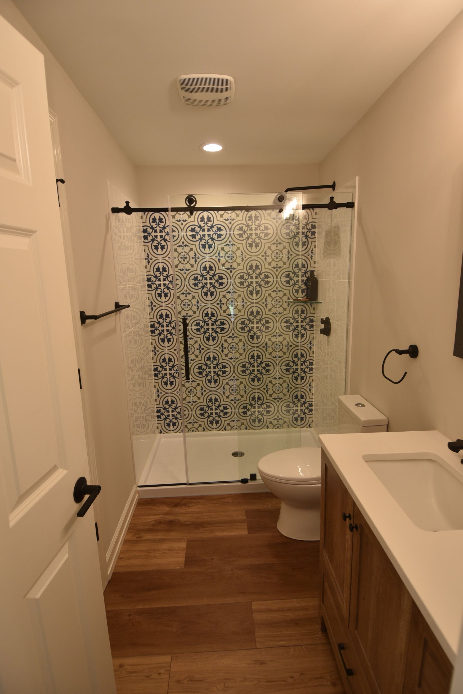 Bathroom with wood-look floor, white walls, blue tile shower, and a wood vanity.