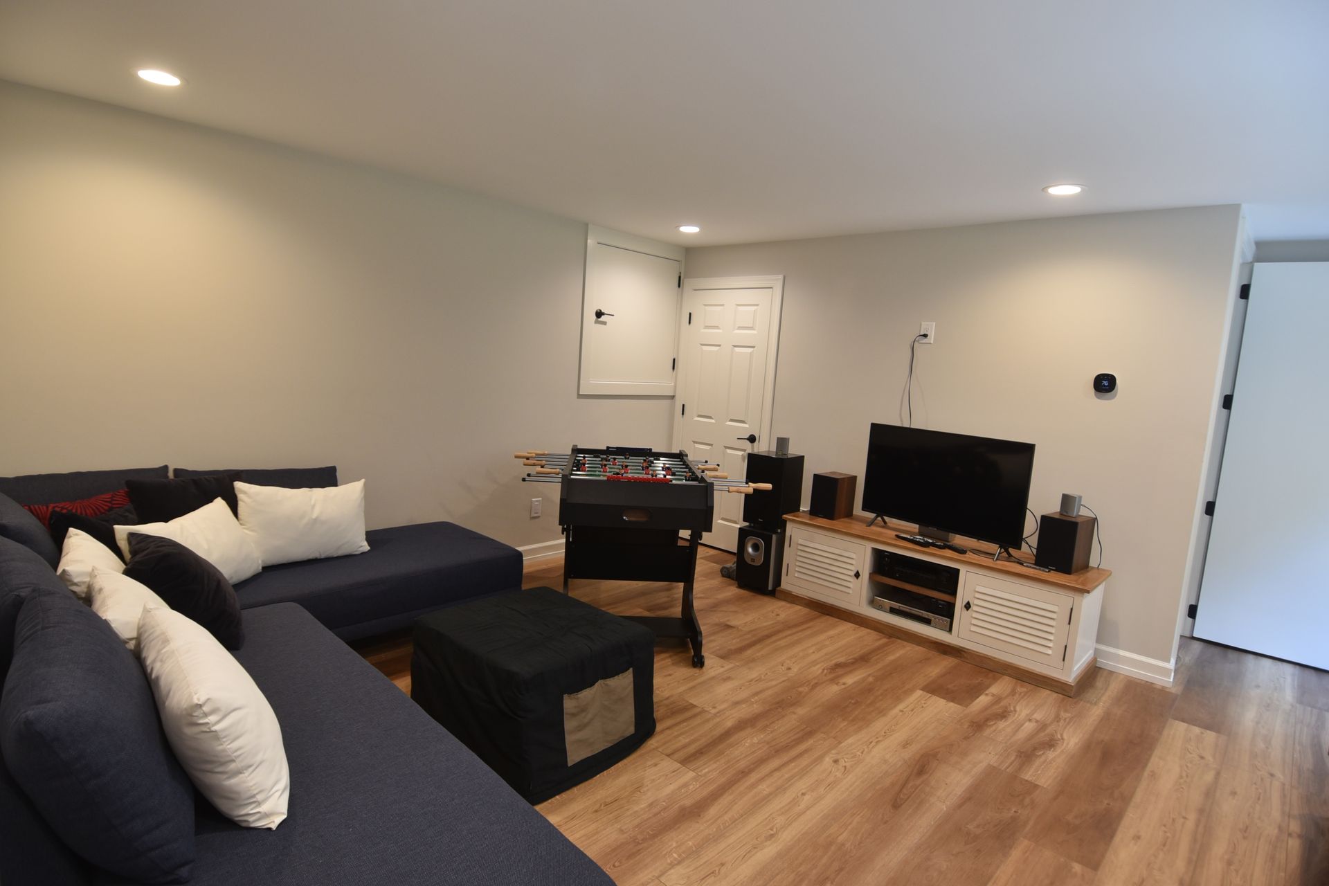 Modern living room with blue sectional sofa, foosball table, TV, and hardwood floors.