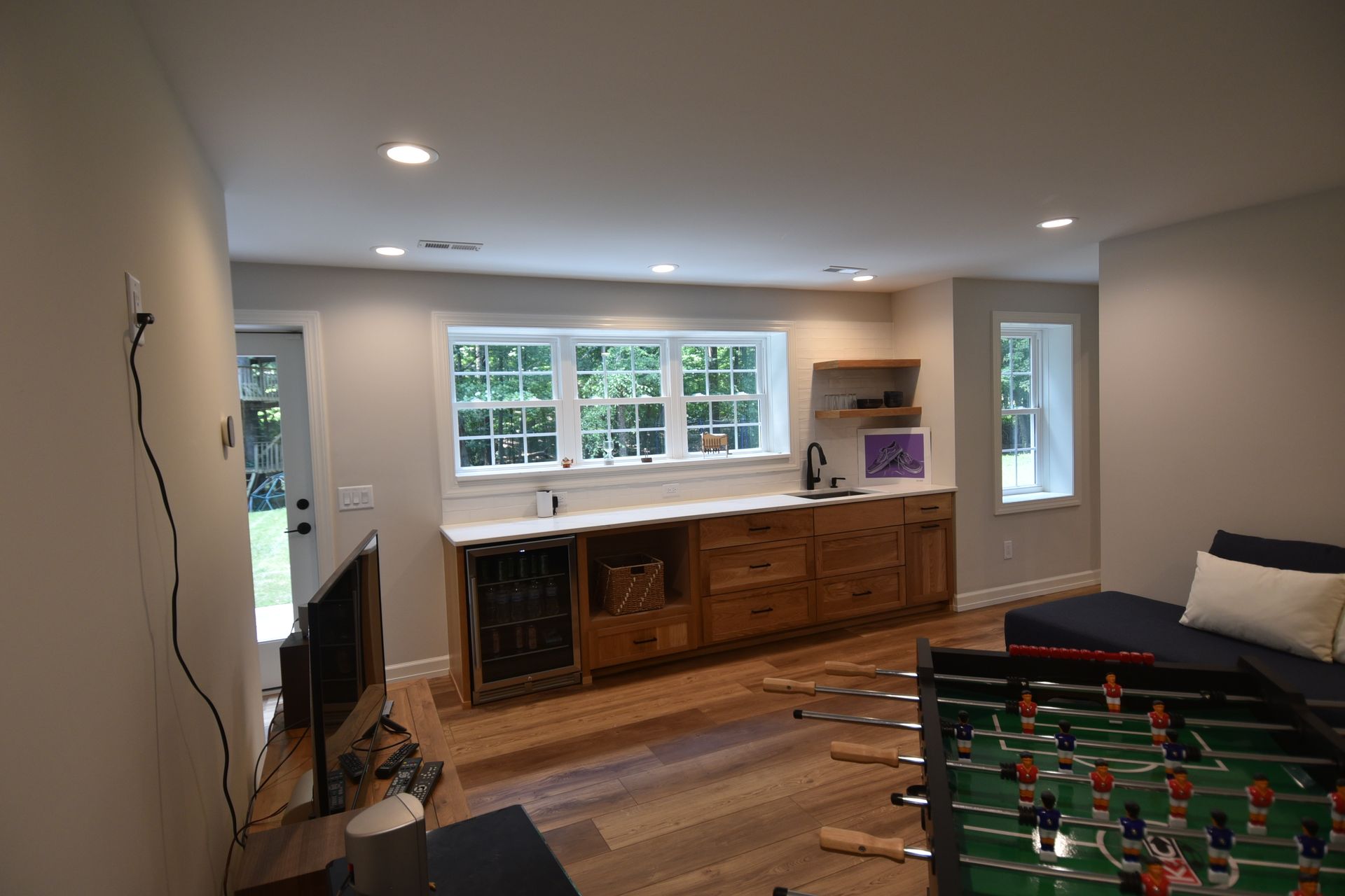 A finished basement with a foosball table, wet bar with wood cabinets, and a sofa.