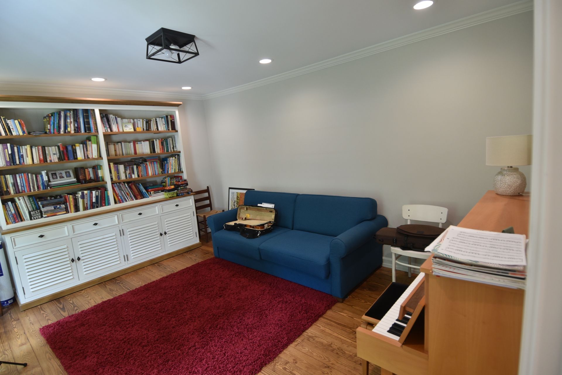 A cozy room with a red rug, blue sofa, bookshelf, piano, and light walls.