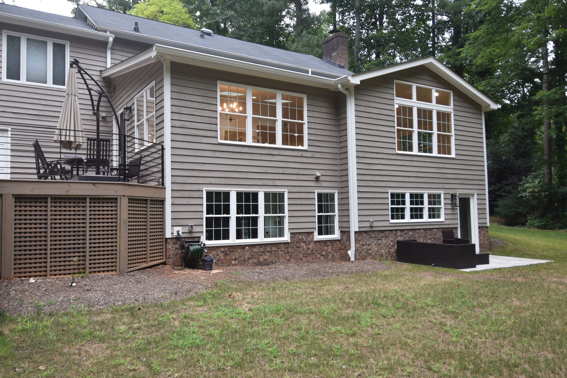 Back of a two-story house with gray siding and white-framed windows; a deck with seating is on the left.