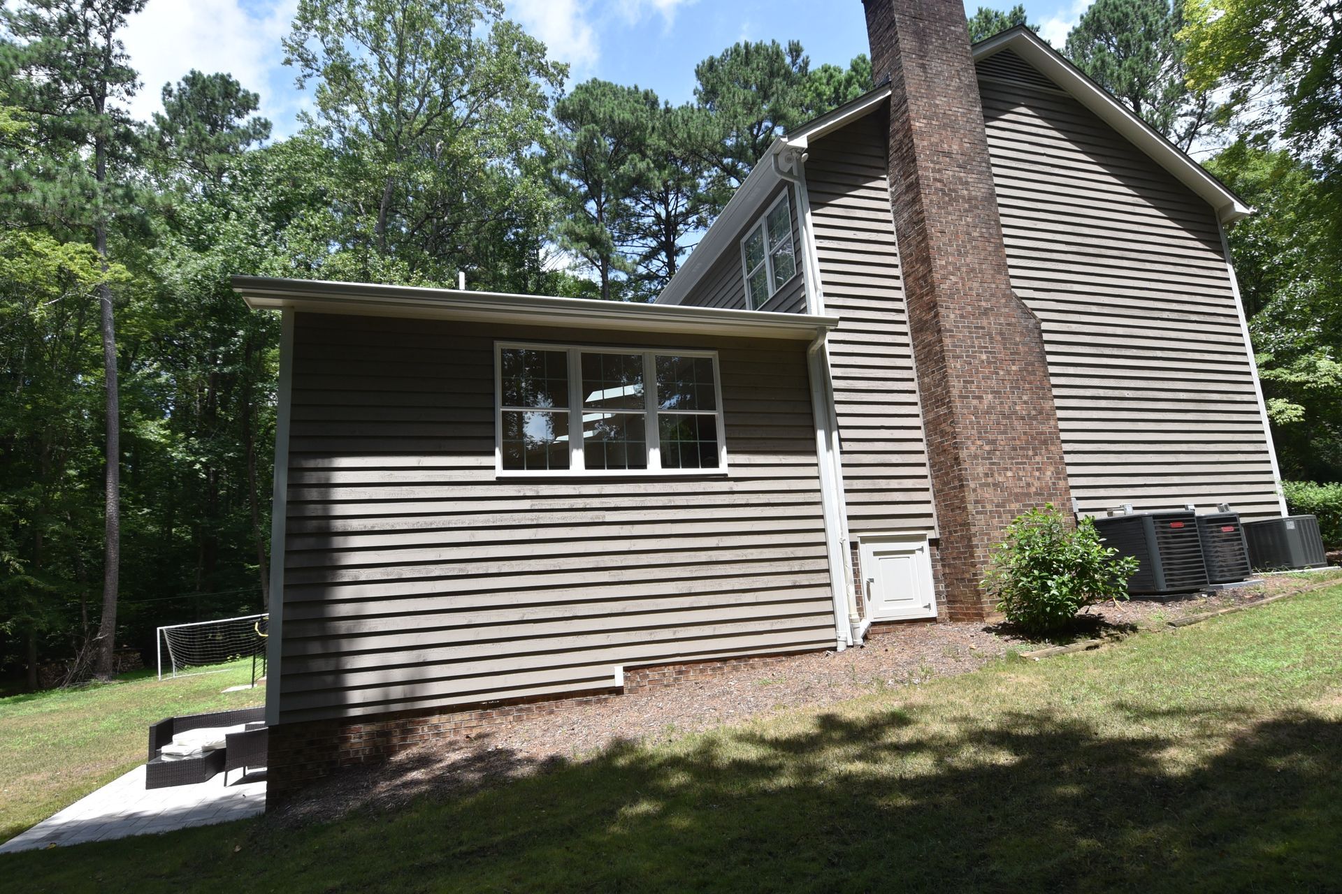 Side view of a brown-sided house with a chimney on a green hillside, with a smaller building attached.