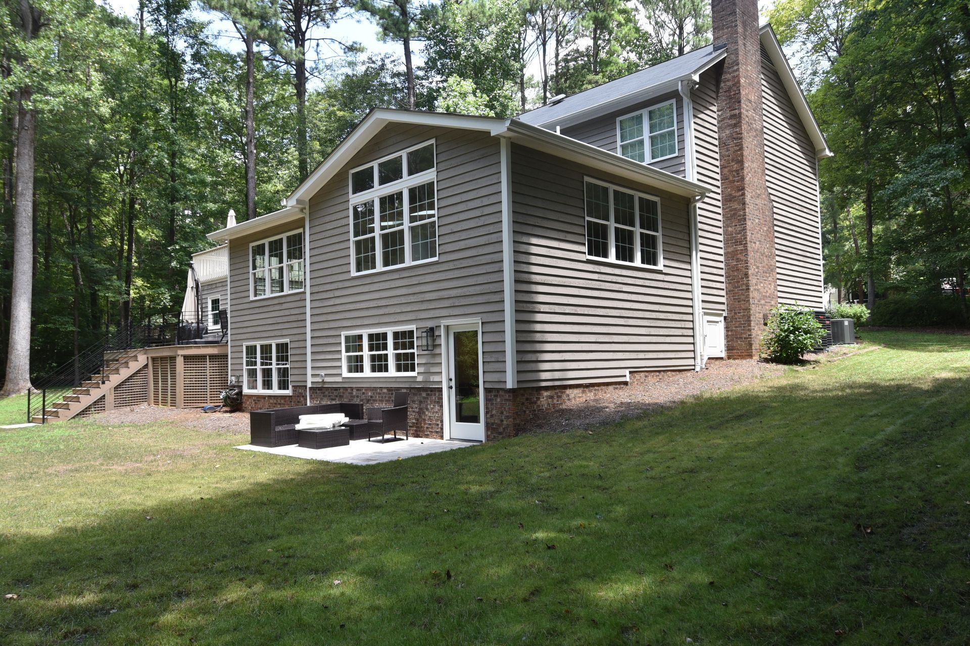Gray house addition with multiple windows, on a grassy slope in a wooded area.