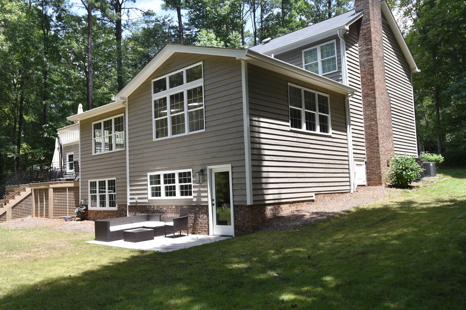 Two-story house with brown siding and brick chimney, white windows, and a green lawn.