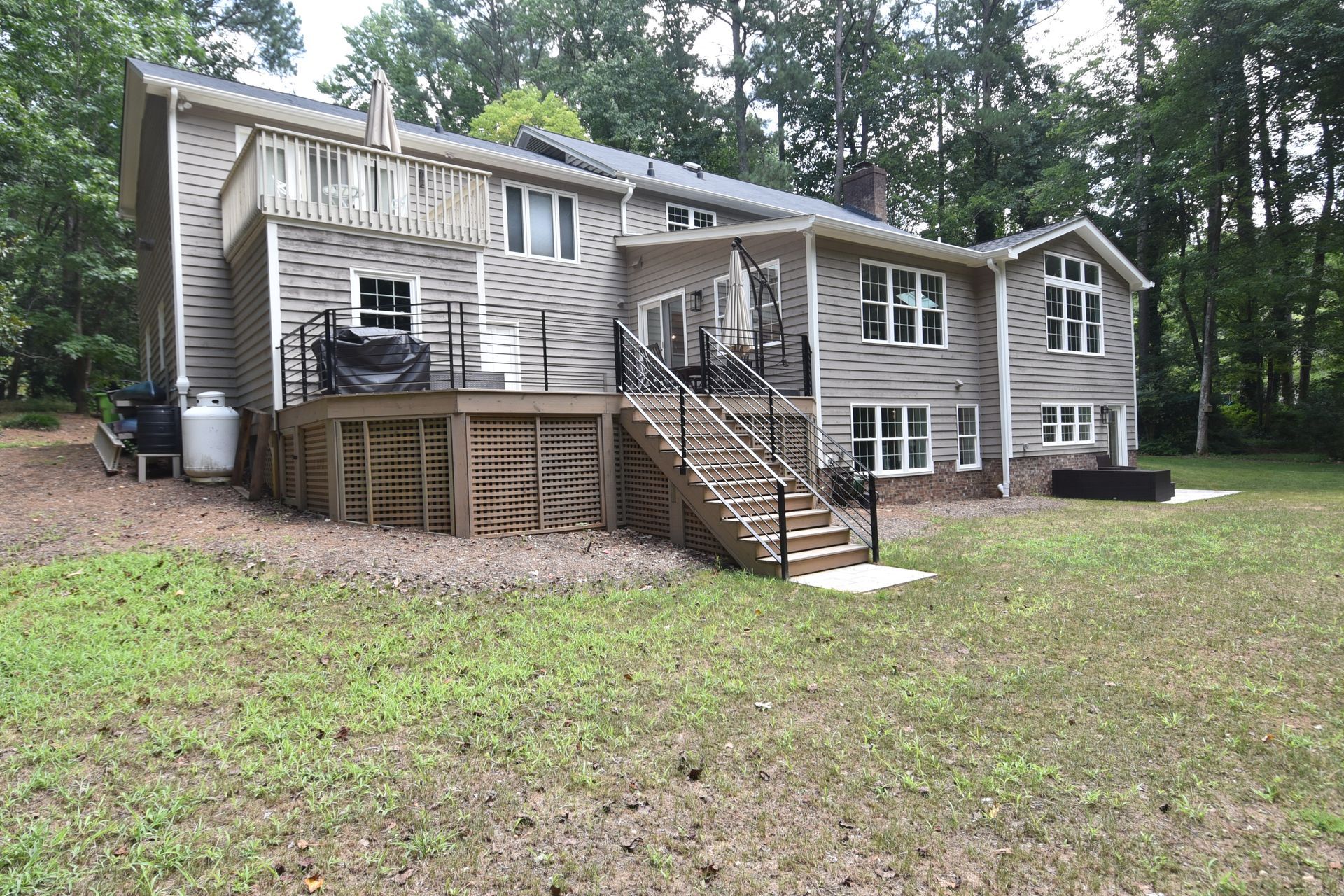 Back of a two-story gray house with multiple decks and a grassy yard surrounded by trees.