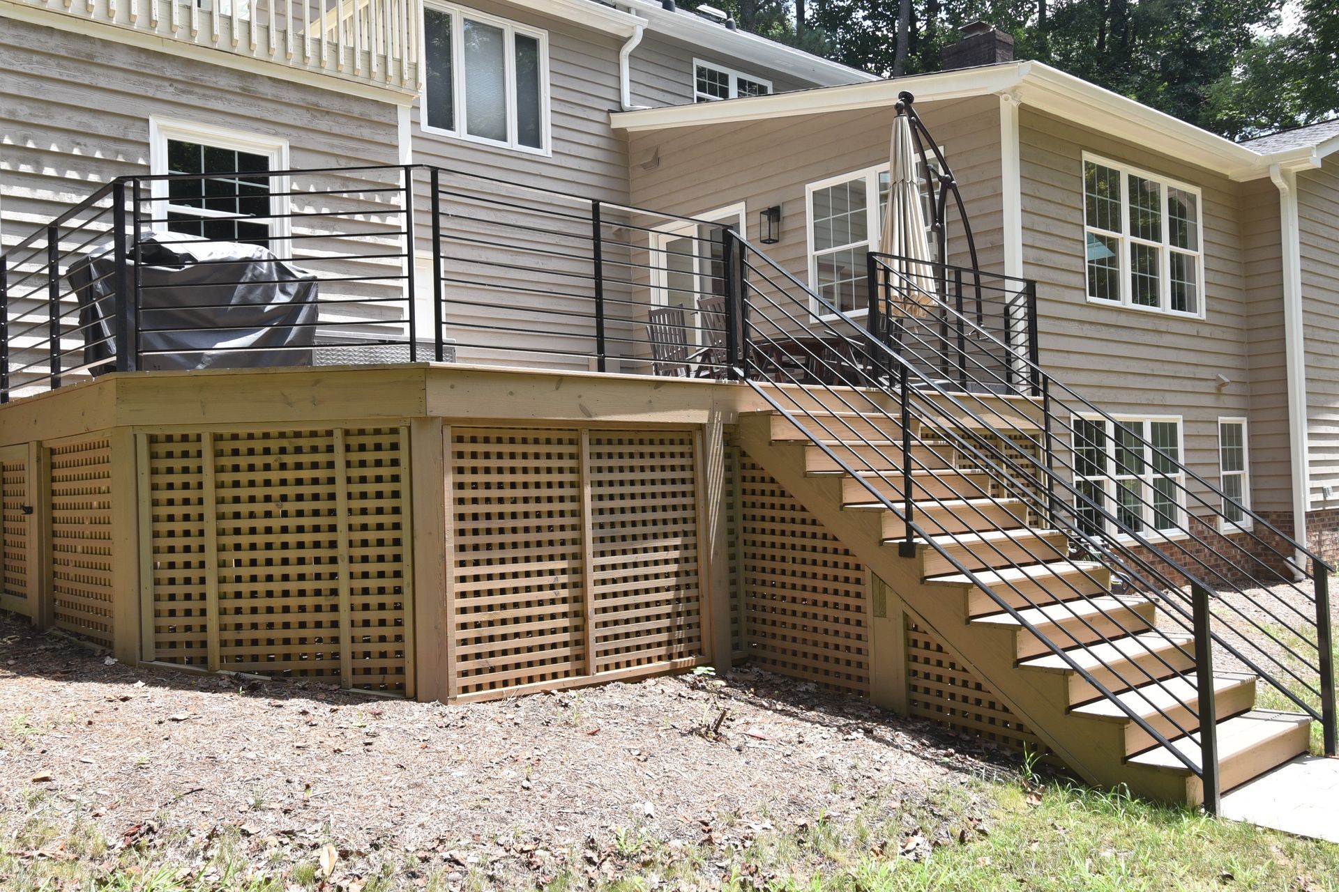 Wooden deck with lattice, stairs, and black railings on a two-story house.