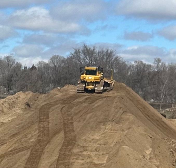 A bulldozer is on top of a pile of sand