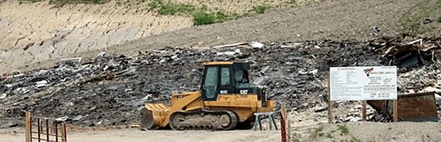 A bulldozer is parked in front of a pile of trash.