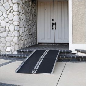 A portable, black and metal ramp placed over two steps leading up to a house's double front doors.
