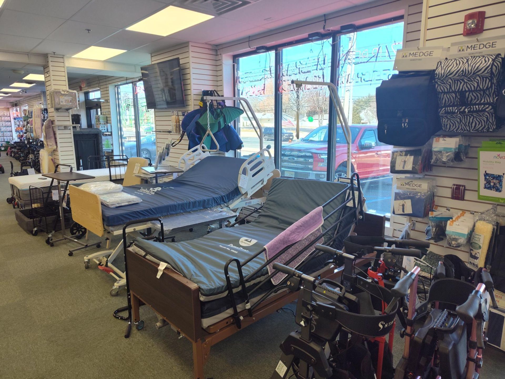 Inside a medical supply store, two hospital beds are displayed. Window shows a car. Shelves with various products.