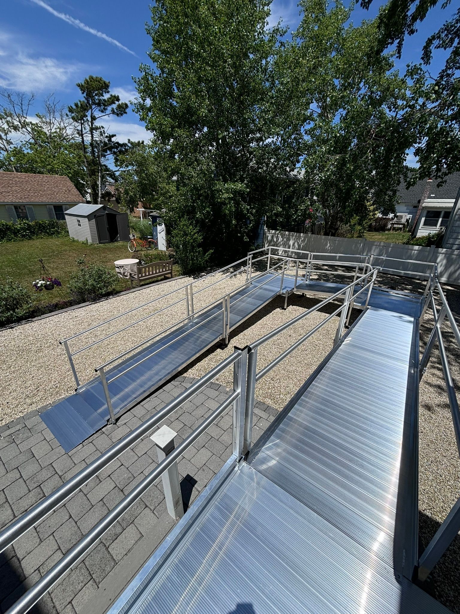Metal ramp with railings provides accessibility. Gravel and trees in the background. Sunny day.