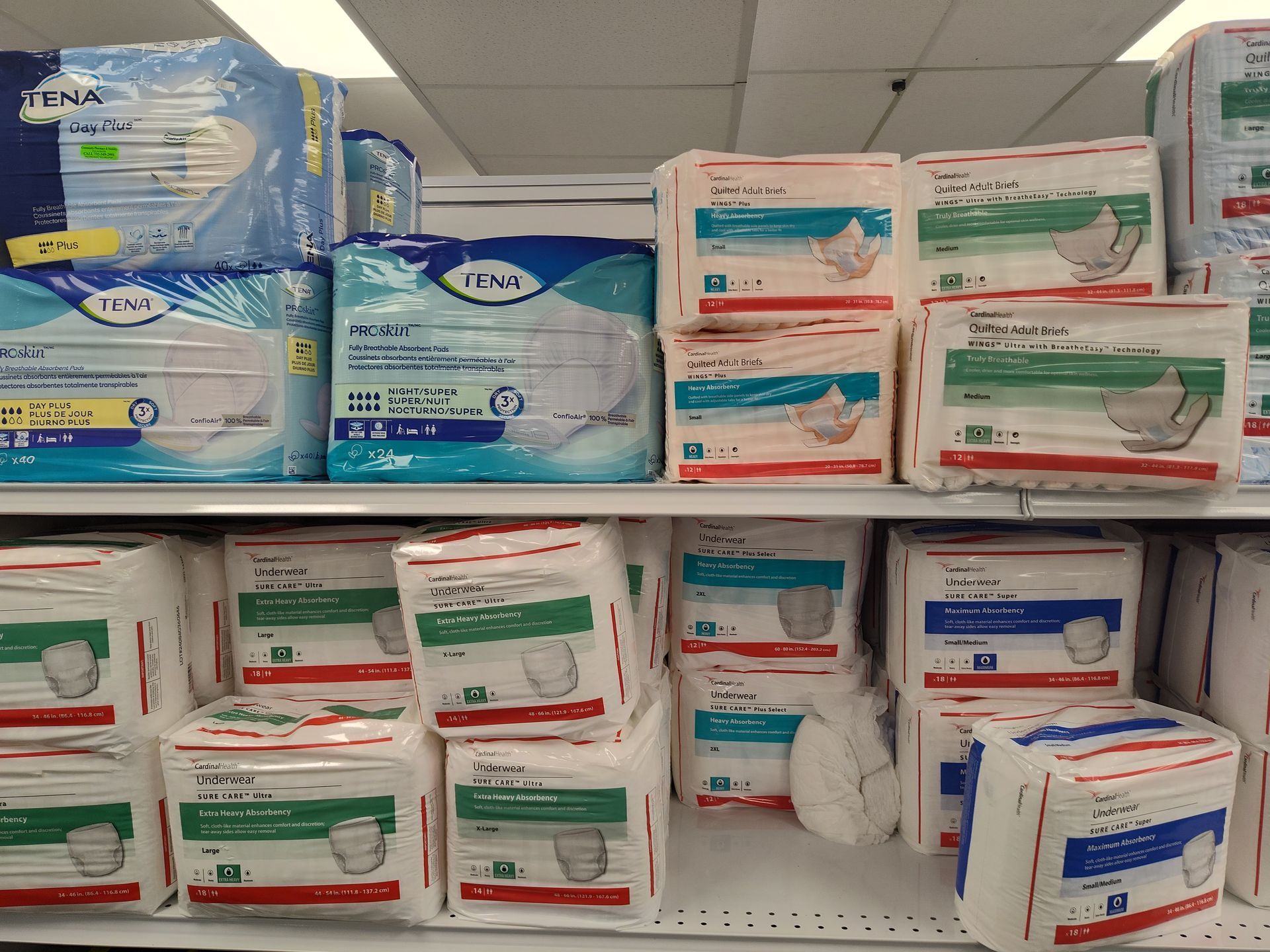 Shelves stocked with various packages of adult incontinence products, featuring blue and white packaging.