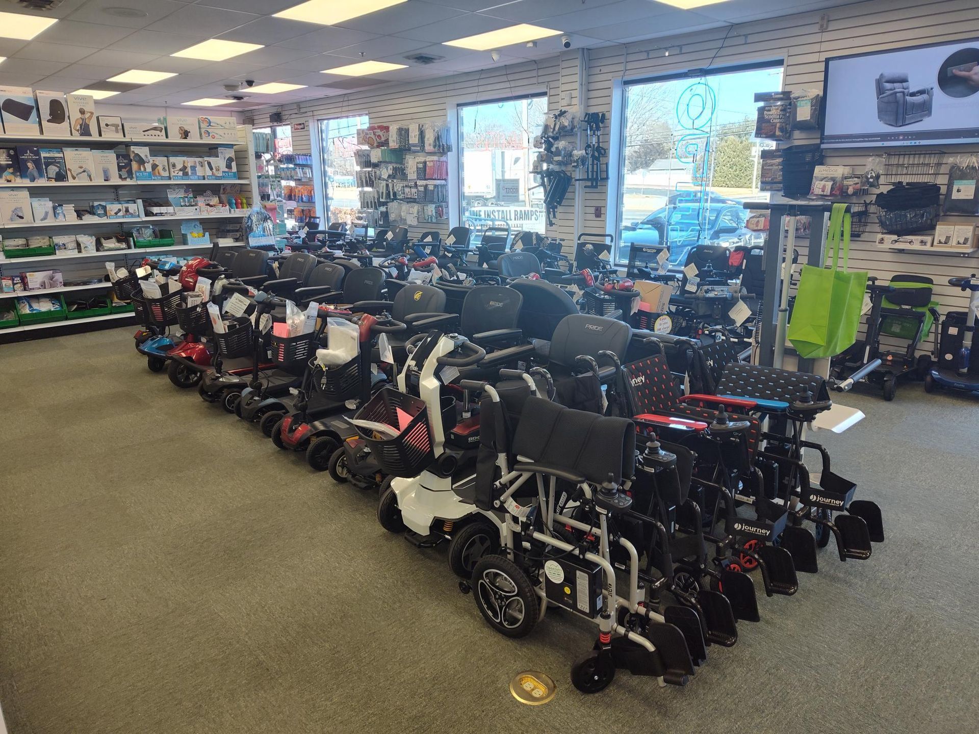 Interior of a mobility equipment store with rows of wheelchairs and scooters. Shelves hold various medical devices; bright lighting.