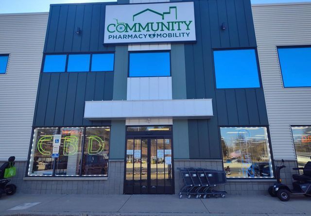 Community Pharmacy & Mobility storefront with blue windows. An electric scooter and a person with a bag are visible outside.
