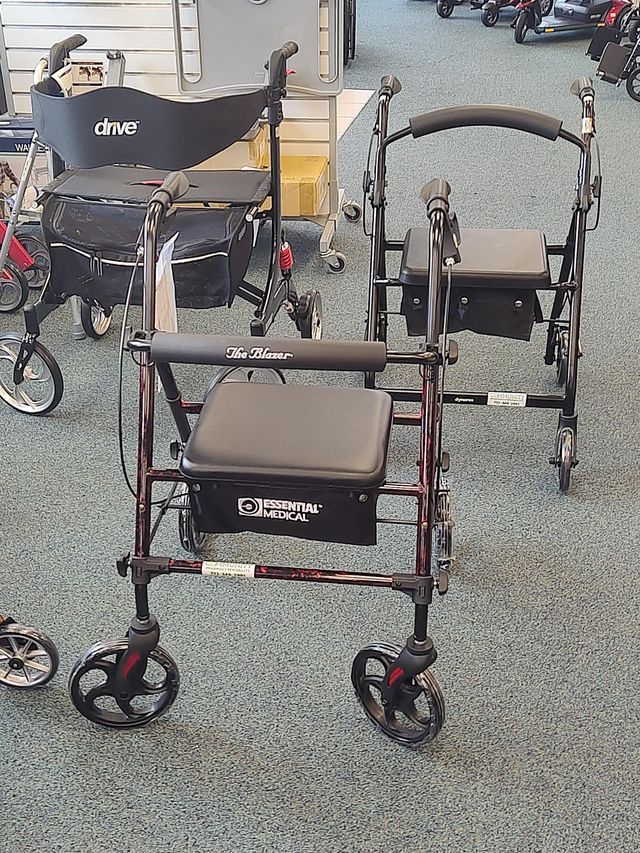 Three burgundy and black rollator walkers with seats and storage, indoors on a patterned floor.