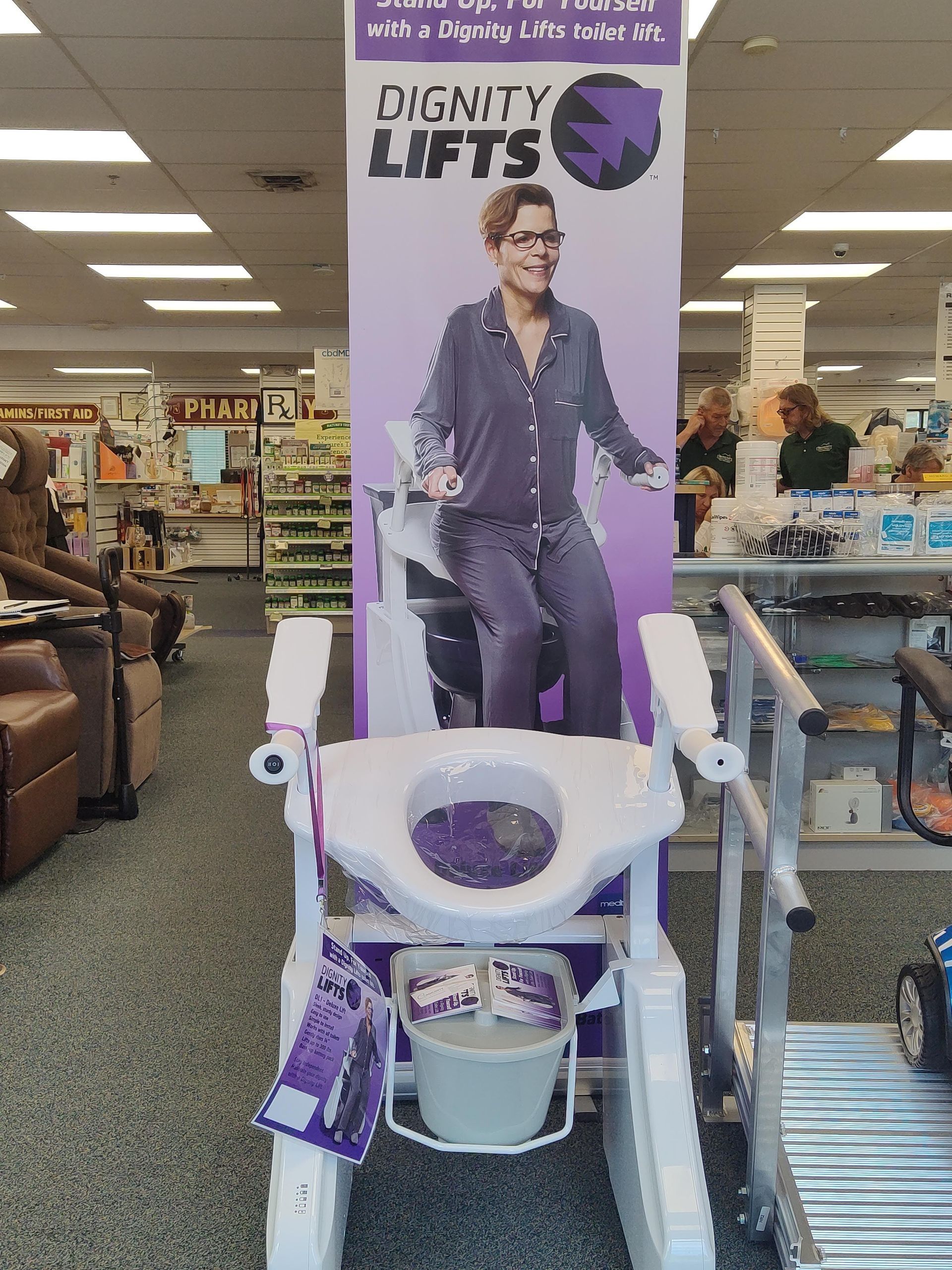 Dignity Lifts toilet aid with a banner featuring a person standing, in a store setting.