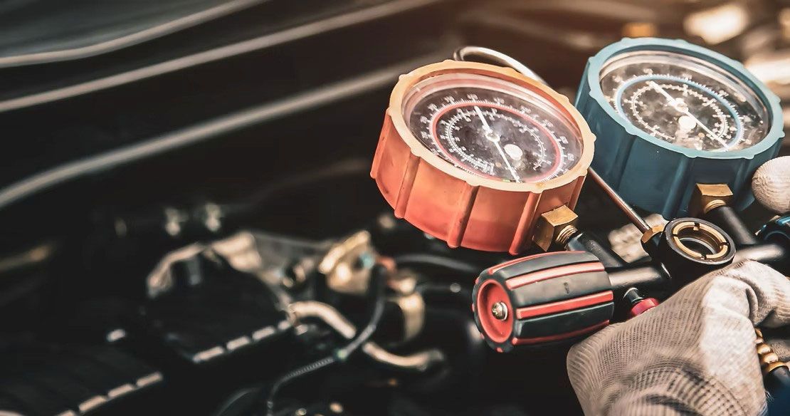 Car dashboard with two vacuum gauge dials and a gloved hand holding a hose attachment