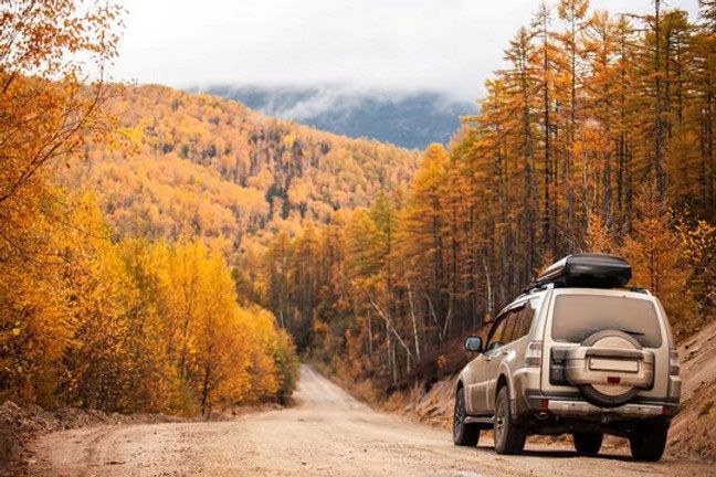 SUV on a dirt road beside autumn trees in a mountain valley