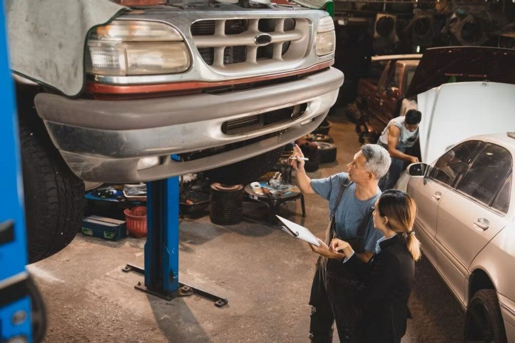 Mechanic inspecting a lifted silver SUV in a busy auto repair shop