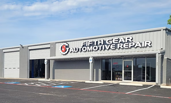 Exterior of a white auto repair shop with a dark sign reading “High Gear Automotive Repair” under a blue sky