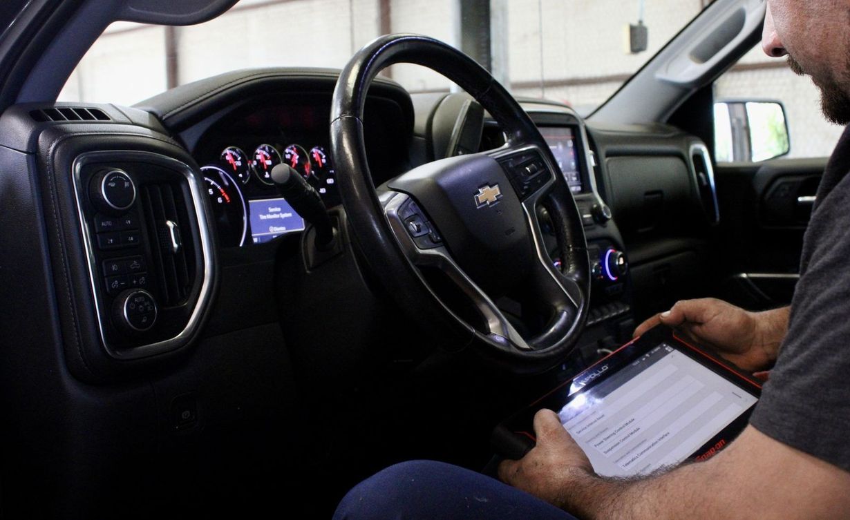 Driver using a steering wheel while a passenger writes on a tablet inside a car