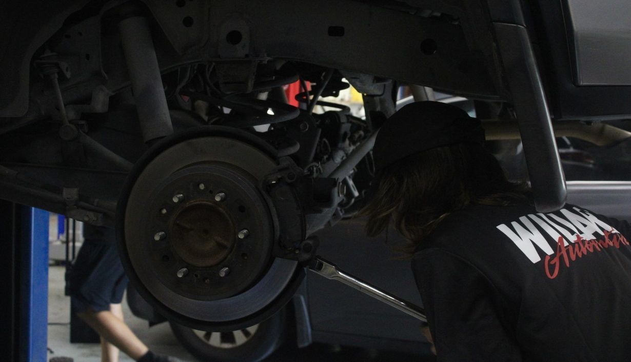 Mechanic working under a car, inspecting the brake assembly in a garage