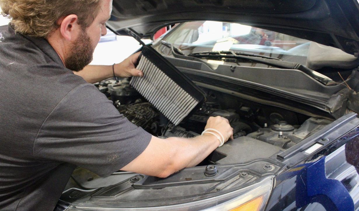 Mechanic replacing a car’s air filter under the open hood of a blue vehicle