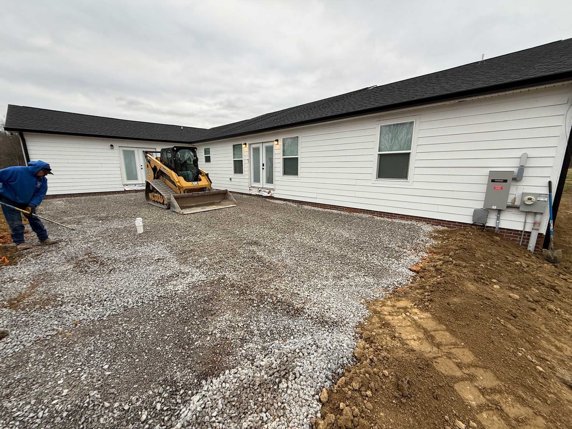 A man is digging a gravel driveway in front of a house.