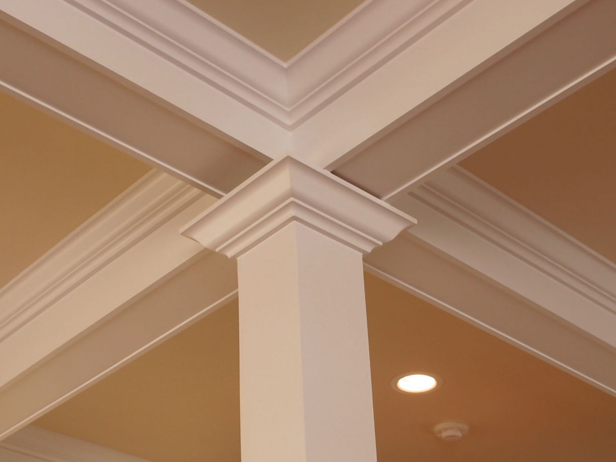 Beige ceiling with intersecting crown molding and a recessed light in a corner