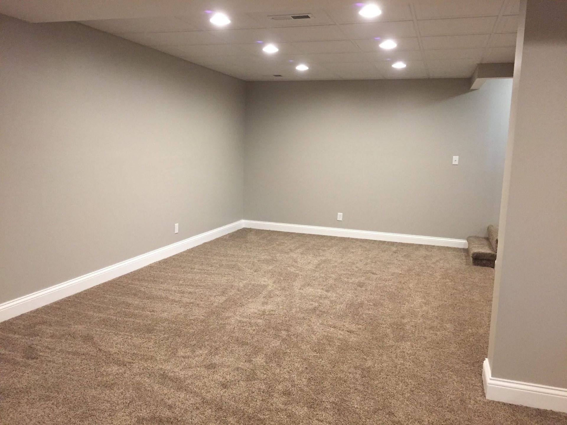Empty carpeted room with gray walls, recessed lights, and a small staircase at the back right.