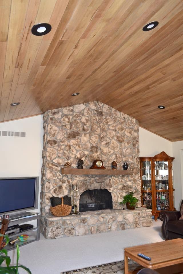 Living room with stone fireplace, wood-paneled ceiling, TV, and glass display cabinet.