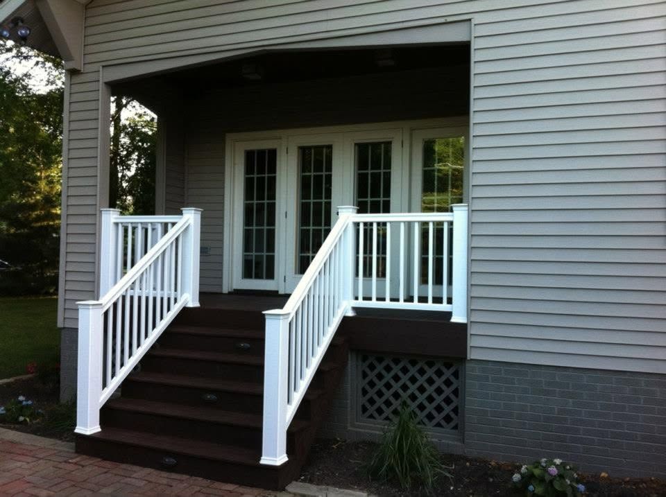 Front porch with white railings and steps leading to double doors on a gray house.